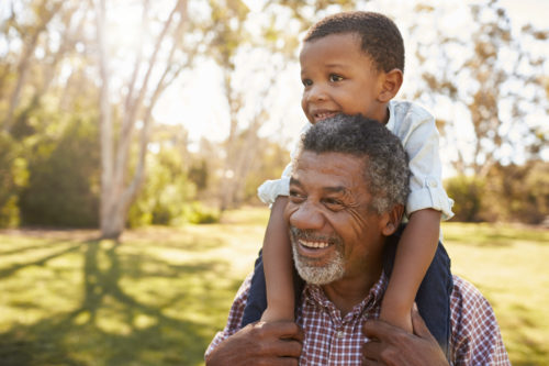 Image of older adult walking with his grandson on his shoulders